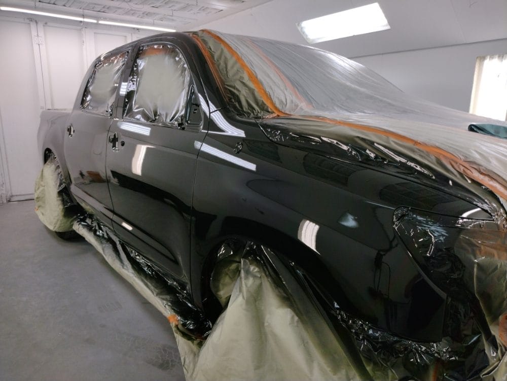 Truck masked for painting with fresh gloss black paint in the spray booth